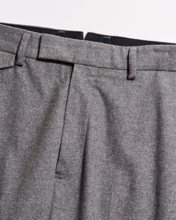 Close-up of the waistband and upper section of a pair of grey dress trousers, showing belt loops, pleats, and part of the zipper area against a plain background.