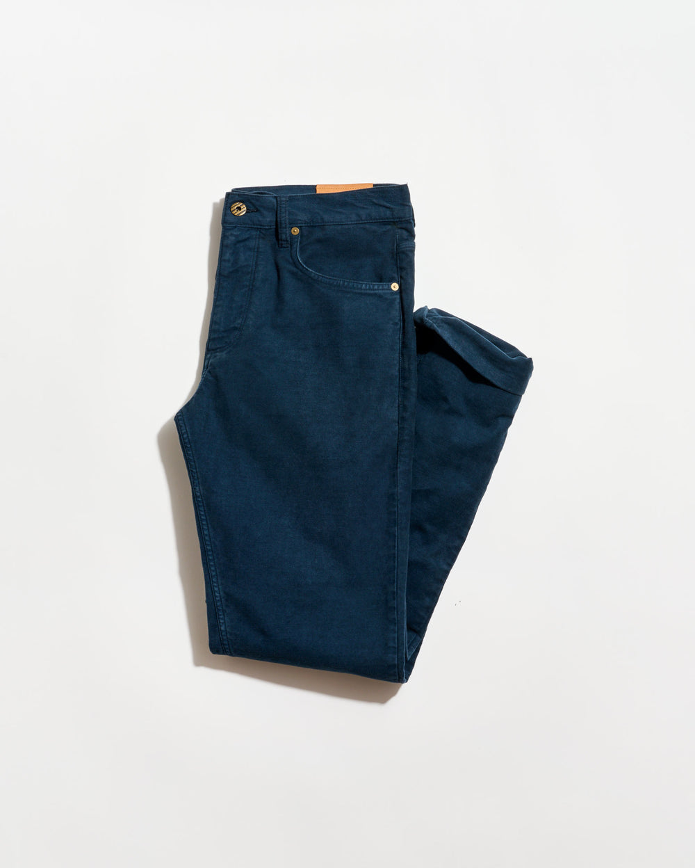 A pair of neatly folded dark blue jeans with visible front pockets and a brown leather patch on the waistband, displayed on a plain white background.