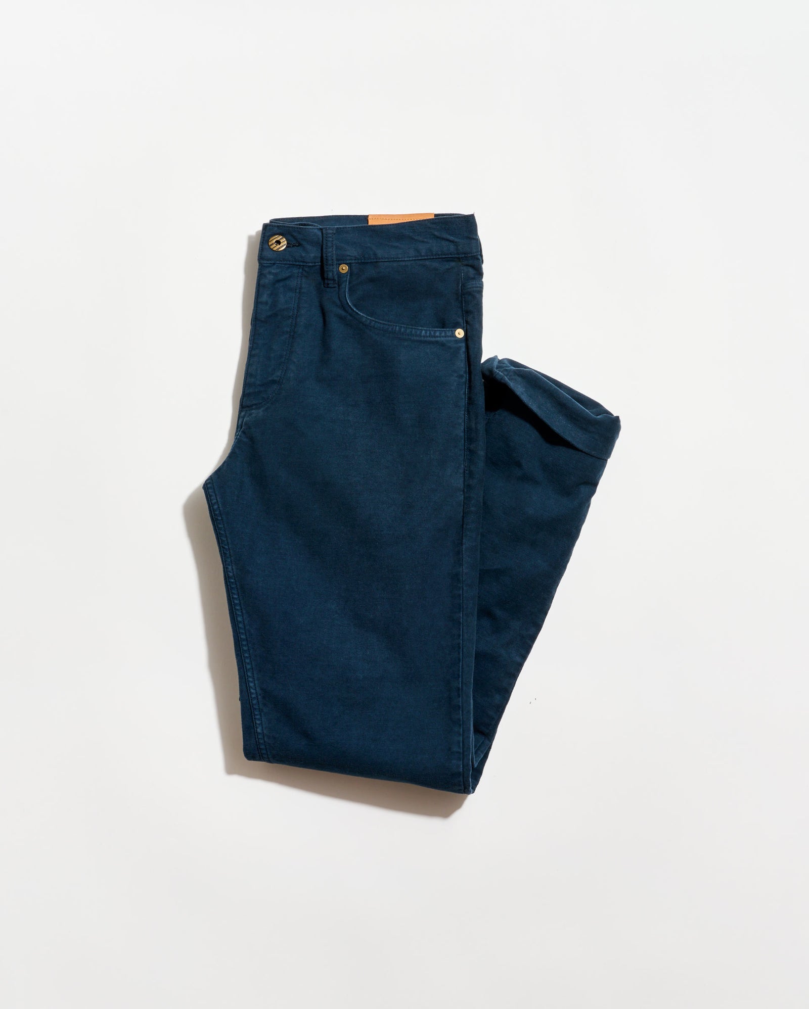 A pair of neatly folded dark blue jeans with visible front pockets and a brown leather patch on the waistband, displayed on a plain white background.