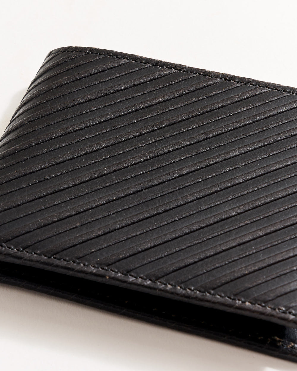 A close-up of a black leather wallet with diagonal textured lines, partially visible against a white background.