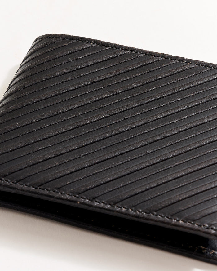A close-up of a black leather wallet with diagonal textured lines, partially visible against a white background.