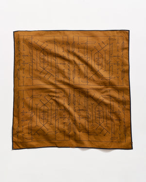 A brown square cloth with a black geometric and linear tribal pattern, bordered by a thin black edge, laid flat on a white background.