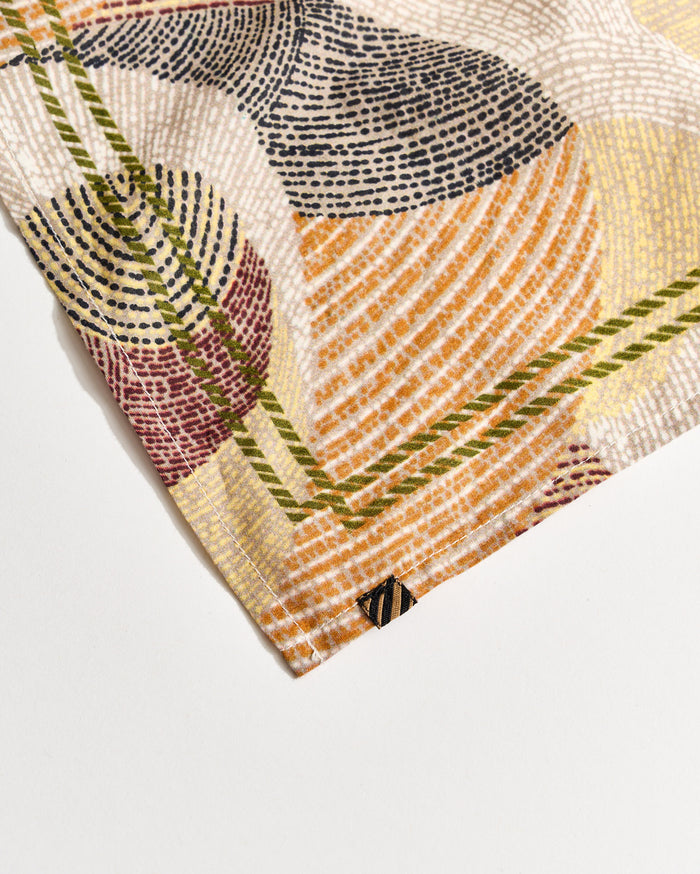 A close-up of a fabric corner with a colorful, abstract geometric pattern in orange, yellow, red, green, black, and white, featuring intersecting curved and straight lines.