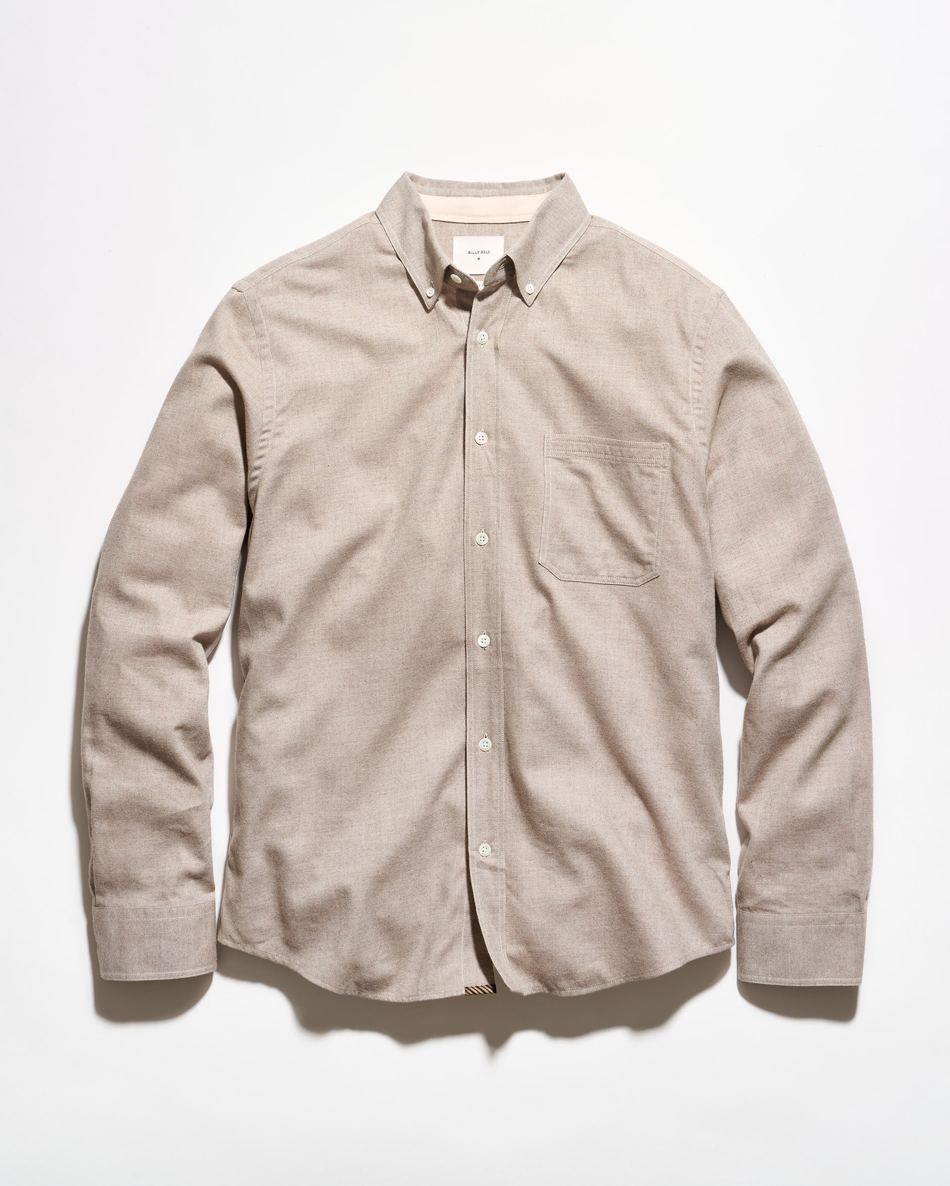 A light beige long-sleeve button-down shirt with a single chest pocket, laid flat against a white background.