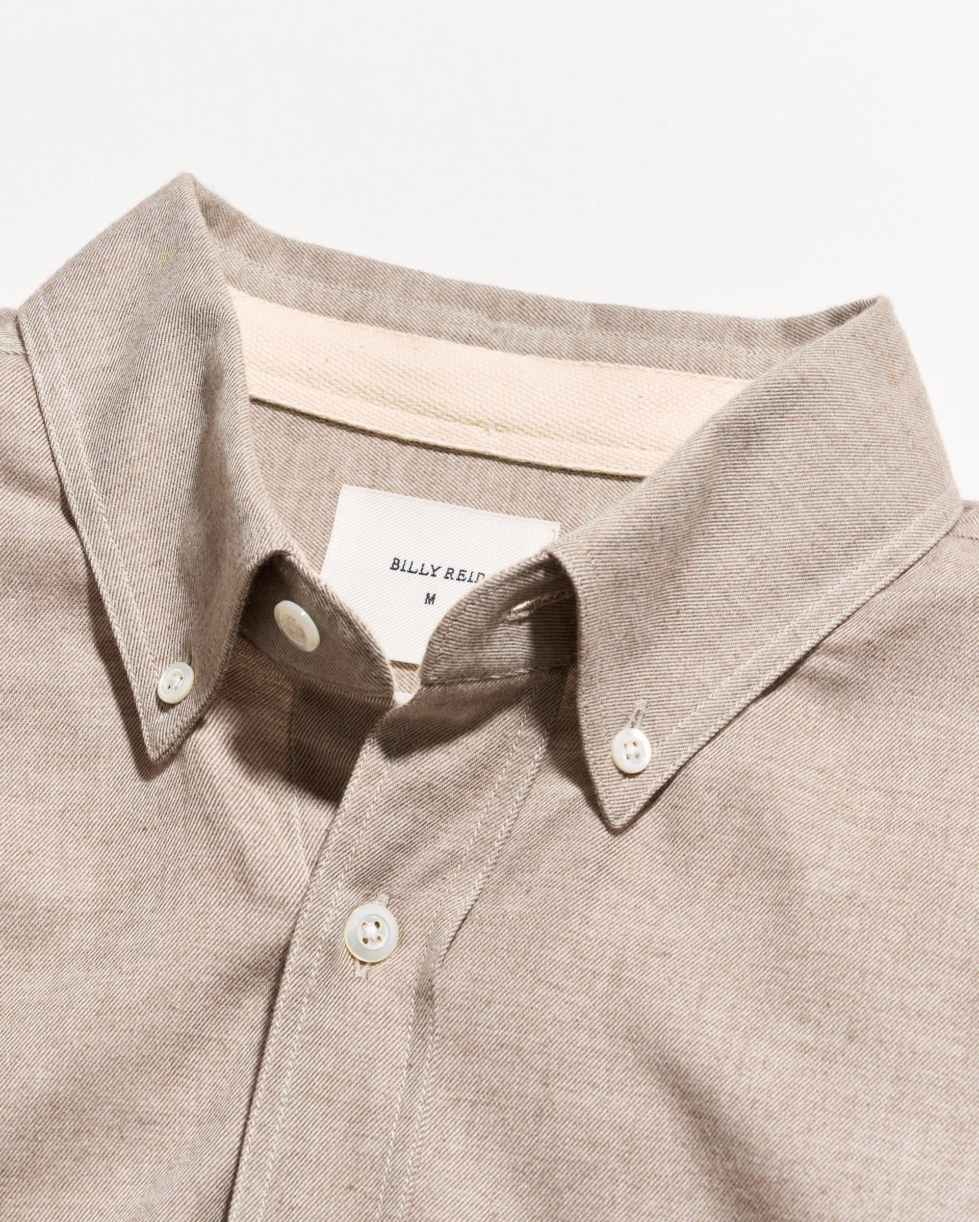 Close-up of a light beige button-down shirt collar with white buttons and a visible Billy Reid neck label.
