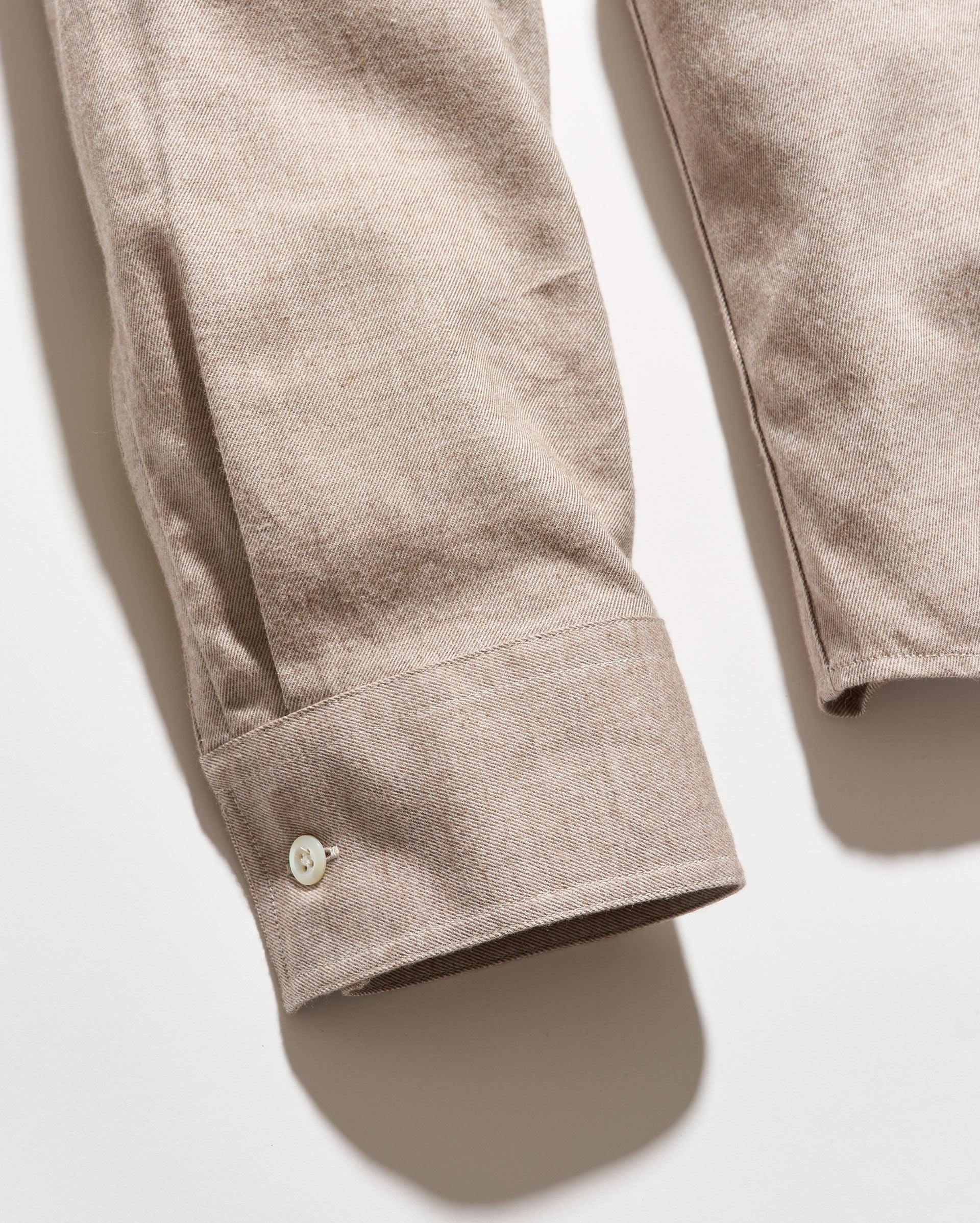 Close-up of a beige cotton shirt sleeve with a buttoned cuff, laid flat on a light background.