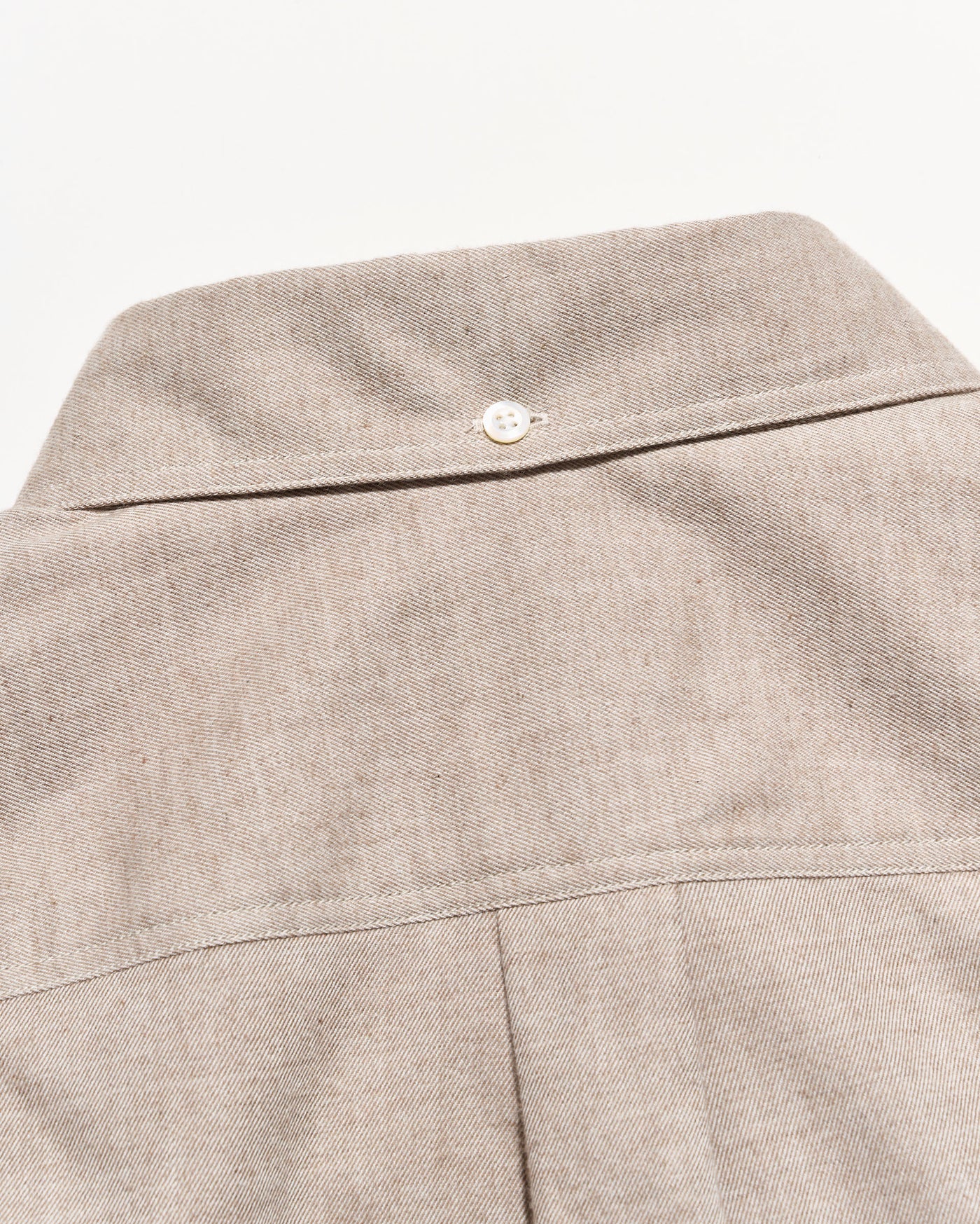 Close-up of a light beige textured fabric garment, showing the back collar with a single white button and a vertical seam below.