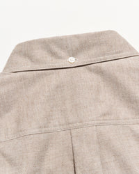 Close-up of a light beige textured fabric garment, showing the back collar with a single white button and a vertical seam below.