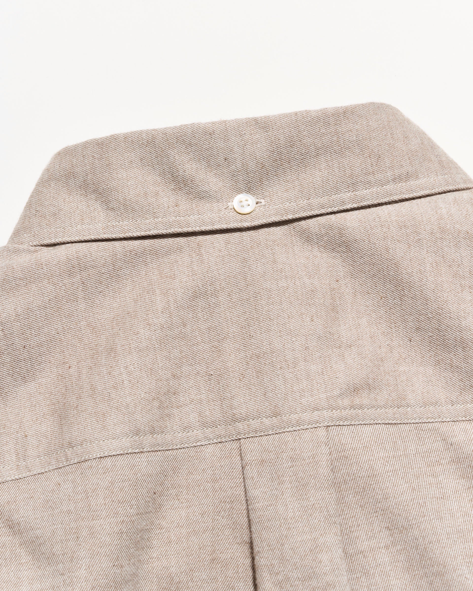 Close-up of a light beige textured fabric garment, showing the back collar with a single white button and a vertical seam below.