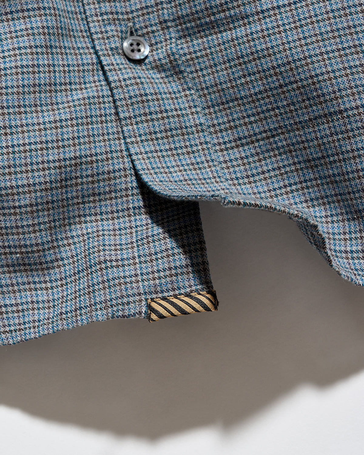 Close-up of a blue and gray plaid shirt fabric with a button and a striped inner lining detail.
