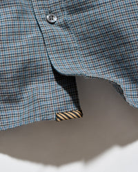 Close-up of a blue and gray plaid shirt fabric with a button and a striped inner lining detail.