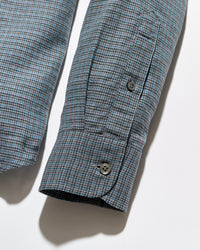 Close-up of a long-sleeve button-up shirt sleeve with a fine blue, gray, and white micro-check pattern, featuring a buttoned cuff and a welt pocket on the upper arm.