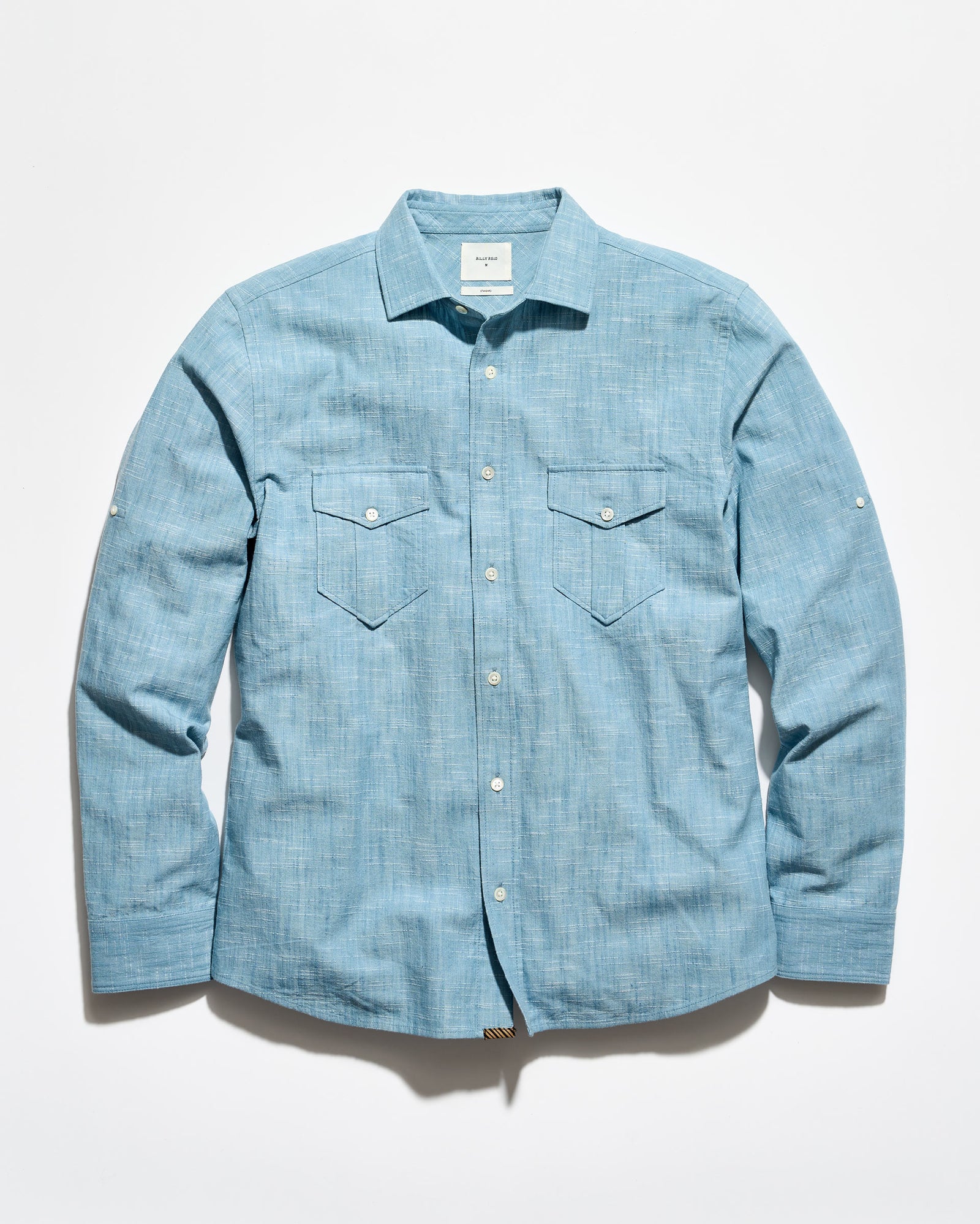 A light blue chambray long-sleeve button-up shirt with two chest flap pockets, laid flat against a white background.