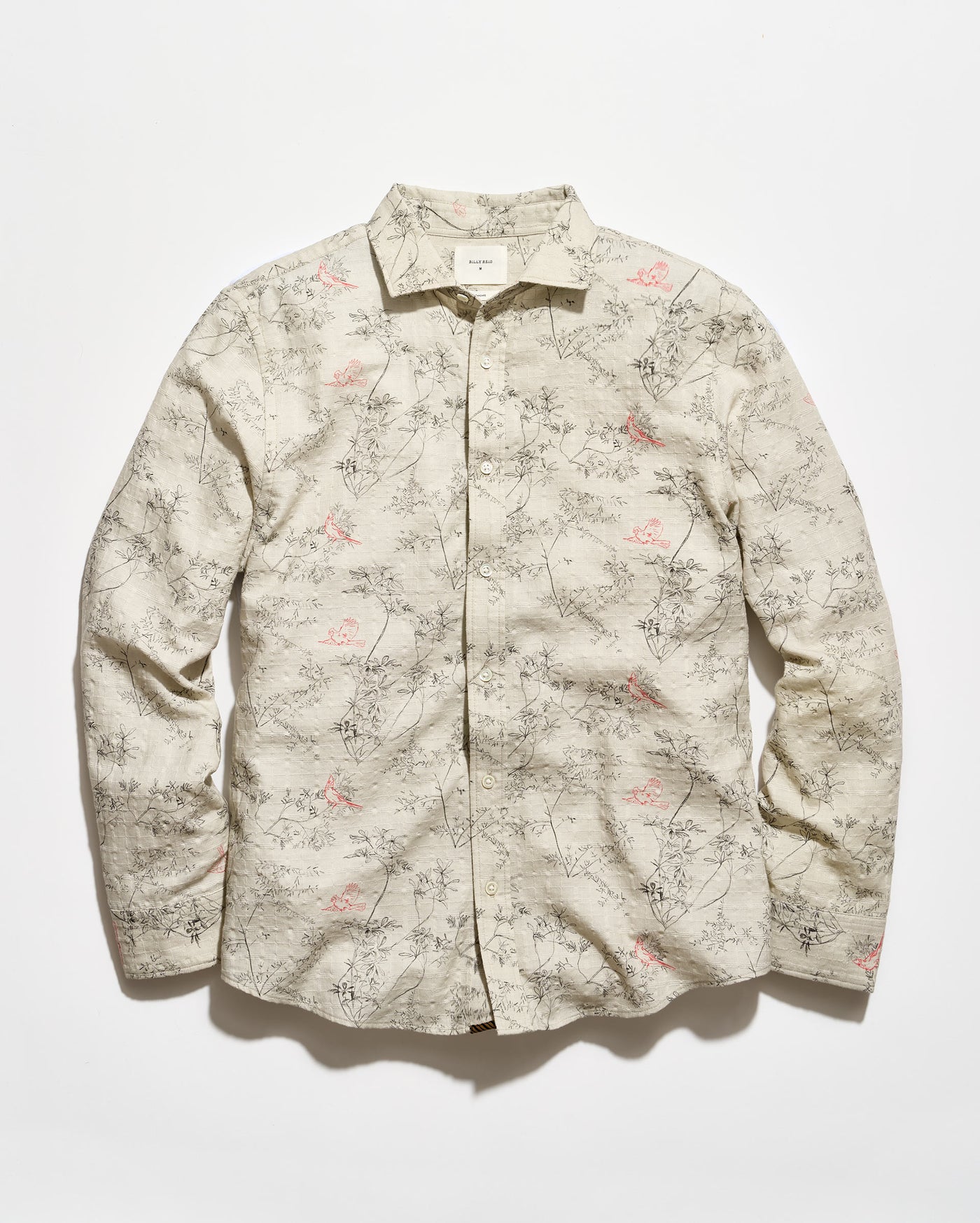A long-sleeve button-up shirt with a beige base and an all-over delicate floral and branch print in muted pink and gray-green, laid flat against a light background.