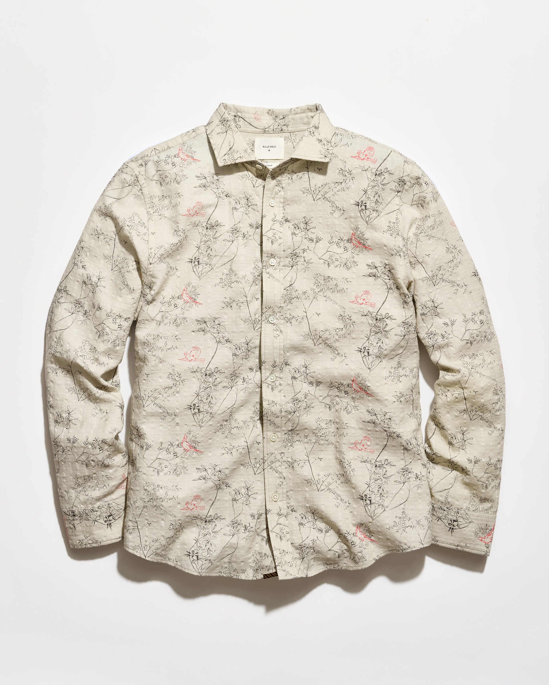 A long-sleeve button-up shirt with a beige base and an all-over delicate floral and branch print in muted pink and gray-green, laid flat against a light background.