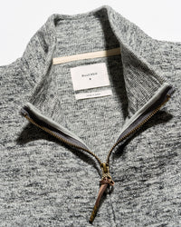 Close-up of a gray heathered knit quarter-zip sweater with a stand collar, showing a white neck label that reads Billie Eilil and a gold-toned zipper.