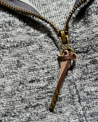 Close-up of a heather gray zippered garment with a decorative bronze zipper pull shaped like a sword or dagger.