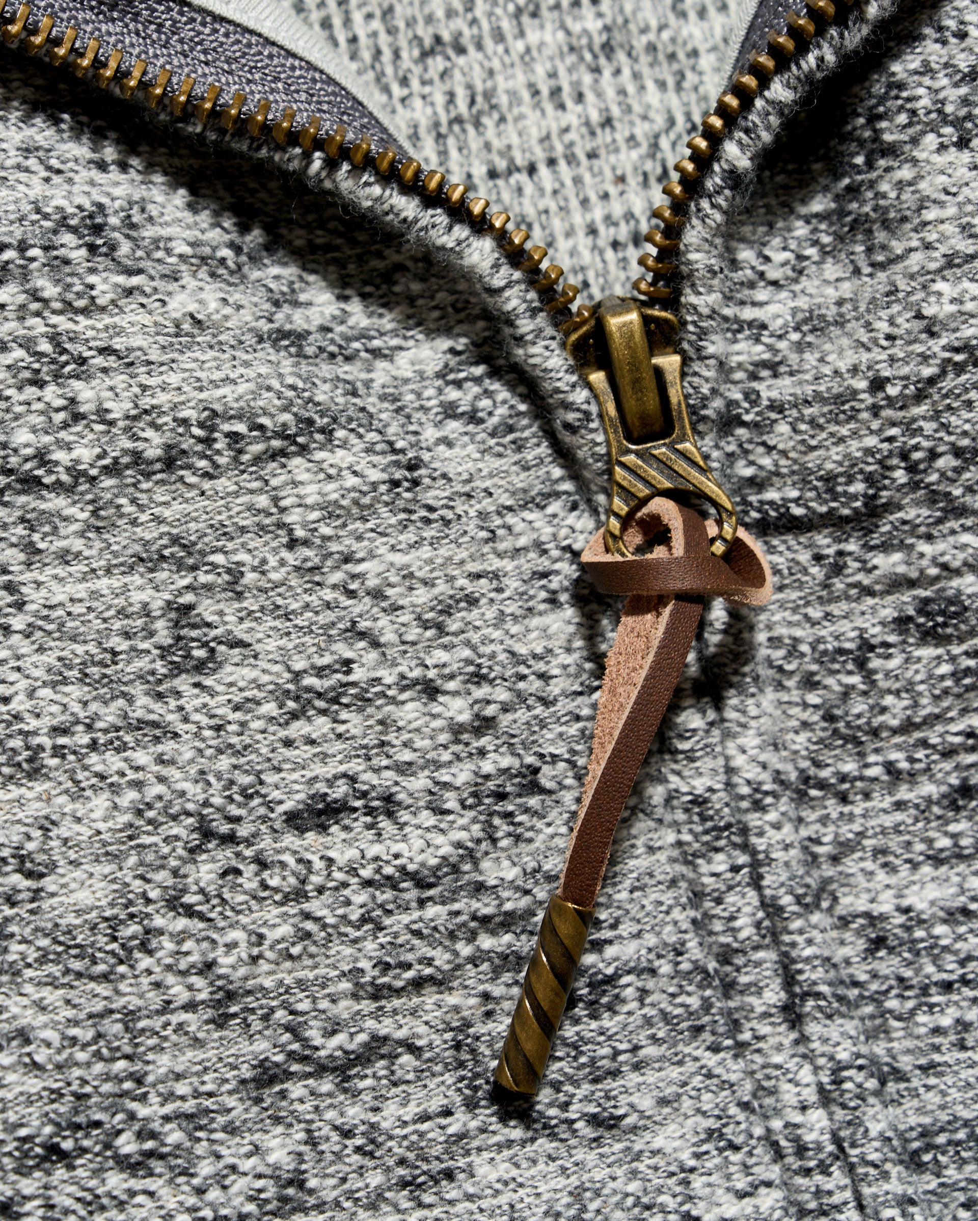 Close-up of a heather gray zippered garment with a decorative bronze zipper pull shaped like a sword or dagger.