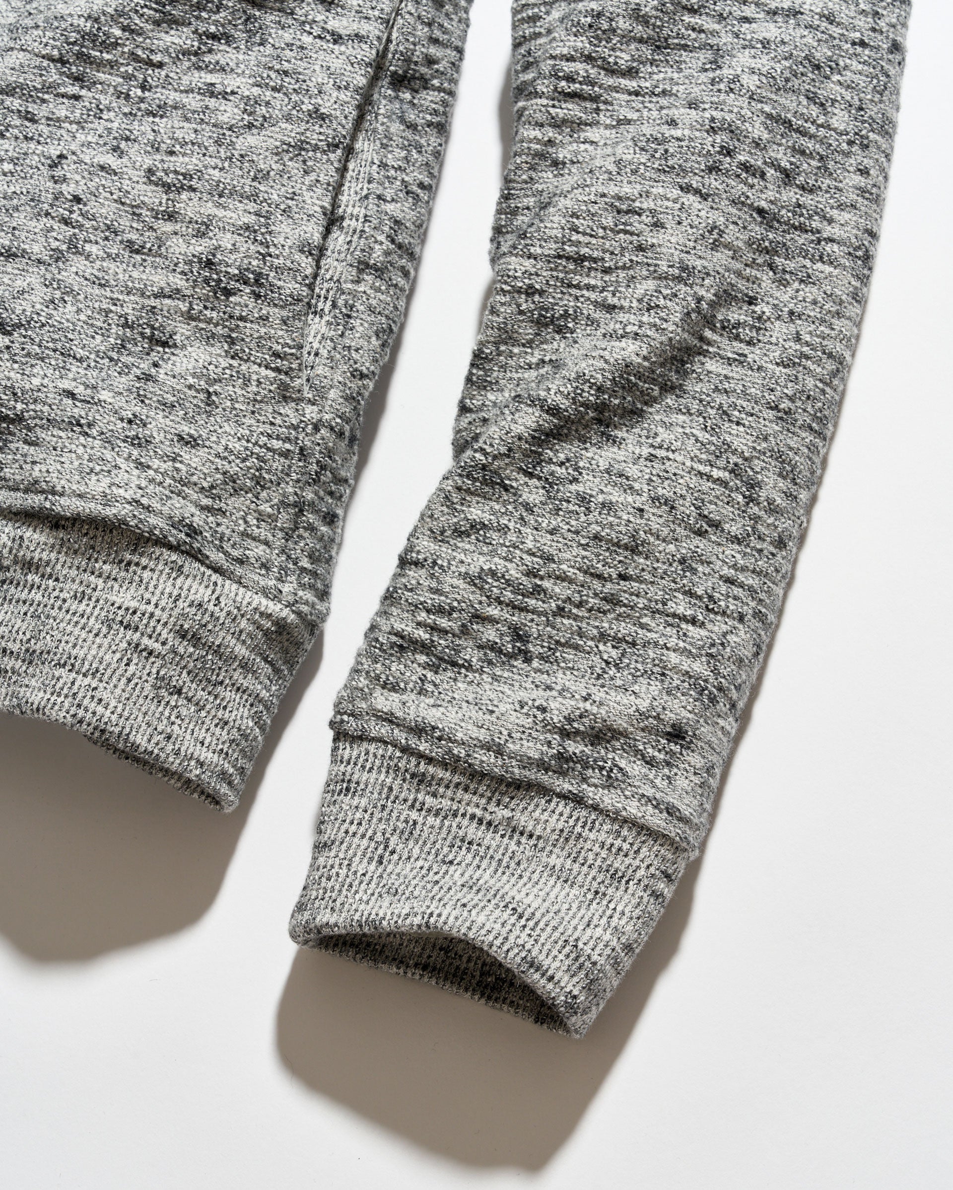 Close-up of a heather gray ribbed knit garment, showing the sleeve cuffs and textured fabric on a light gray background.