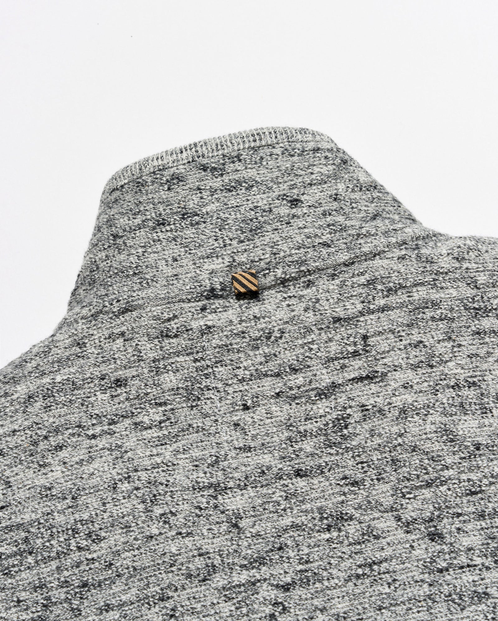 Close-up of a gray and white heather knit sweater or knit garment with a small striped gold and brown button at the neckline, set against a plain light gray background.