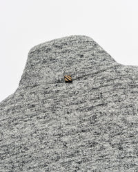 Close-up of a gray and white heather knit sweater or knit garment with a small striped gold and brown button at the neckline, set against a plain light gray background.