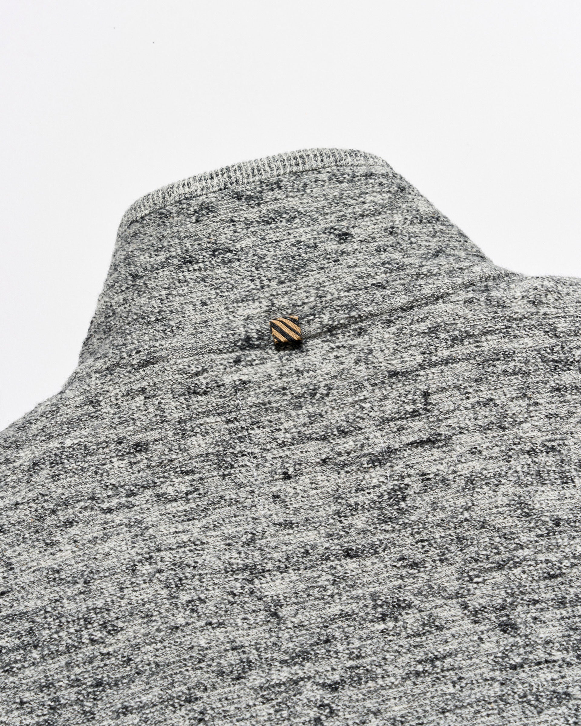 Close-up of a gray and white heather knit sweater or knit garment with a small striped gold and brown button at the neckline, set against a plain light gray background.