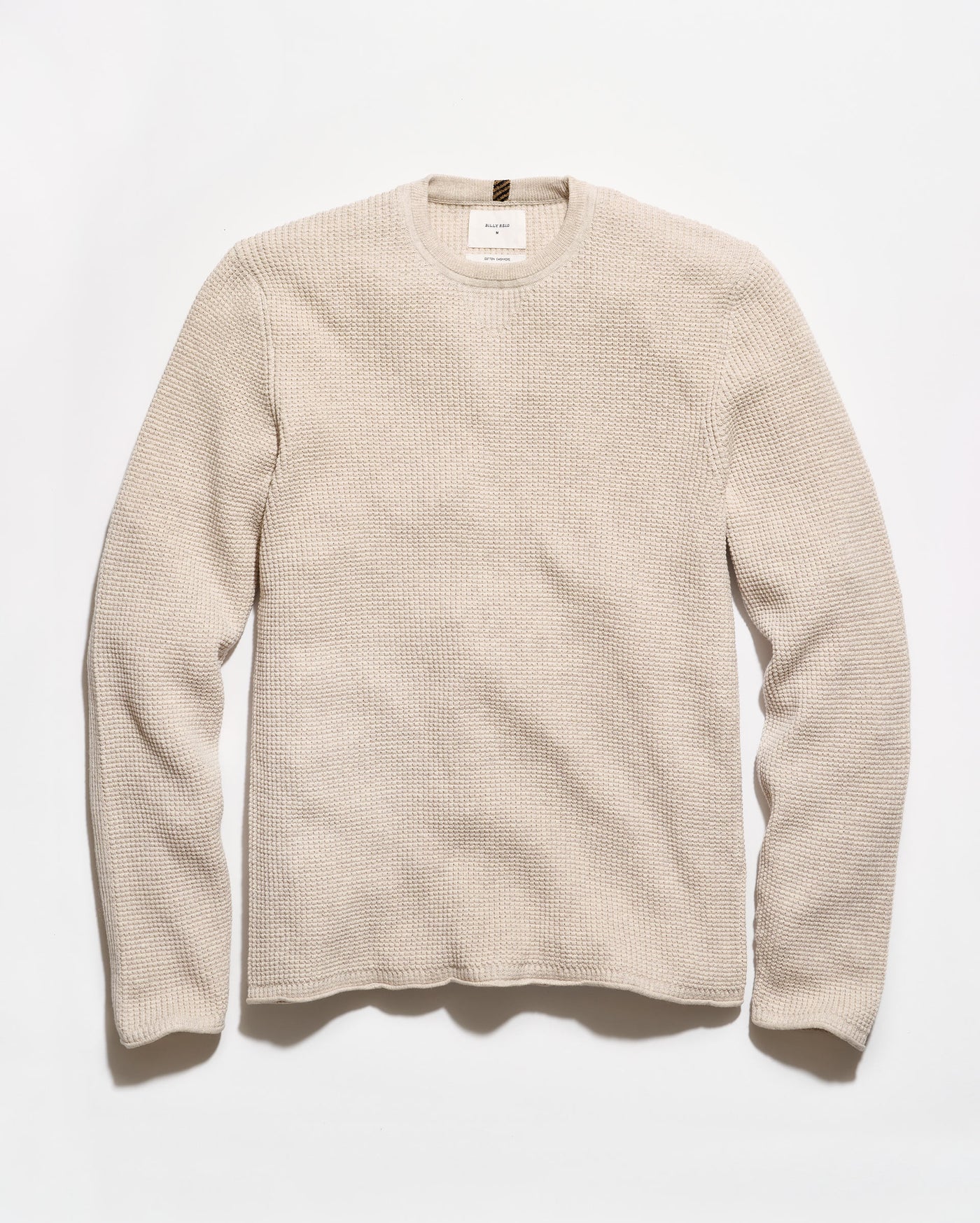 A light beige crewneck sweater with a textured waffle knit pattern, laid flat against a clean white background.