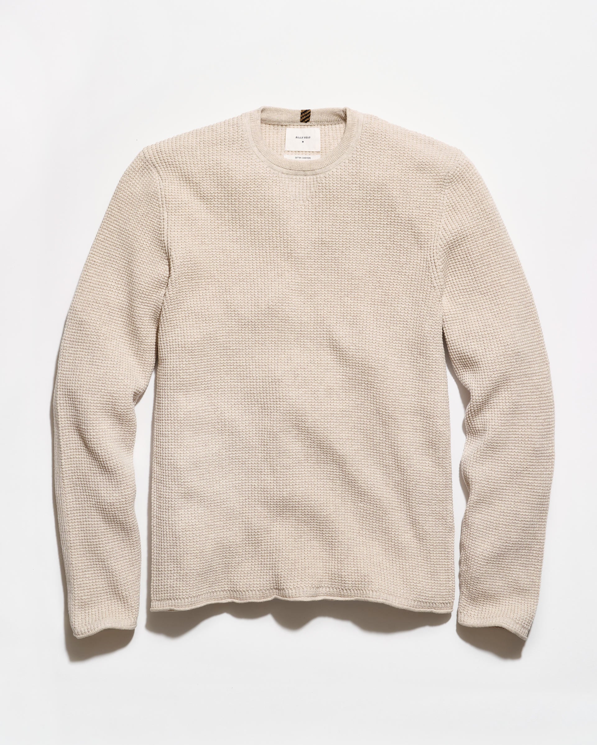 A light beige crewneck sweater with a textured waffle knit pattern, laid flat against a clean white background.