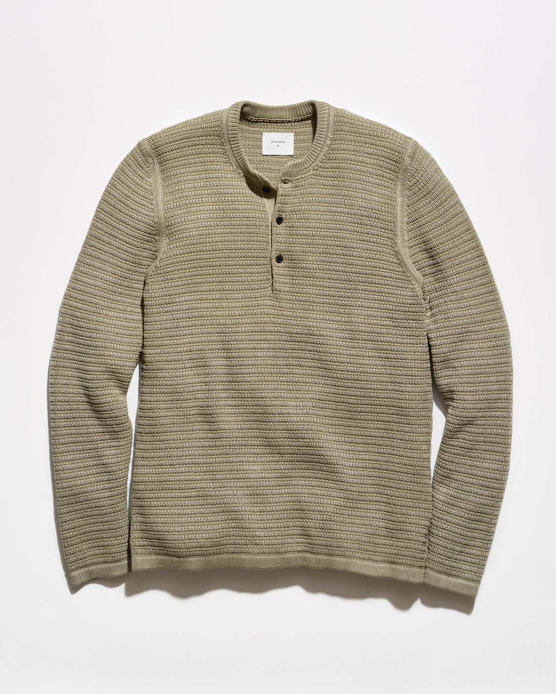 A ribbed knit long-sleeve henley shirt in a muted olive-beige color, featuring a three-button placket and a crew neck, laid flat against a light gray background.