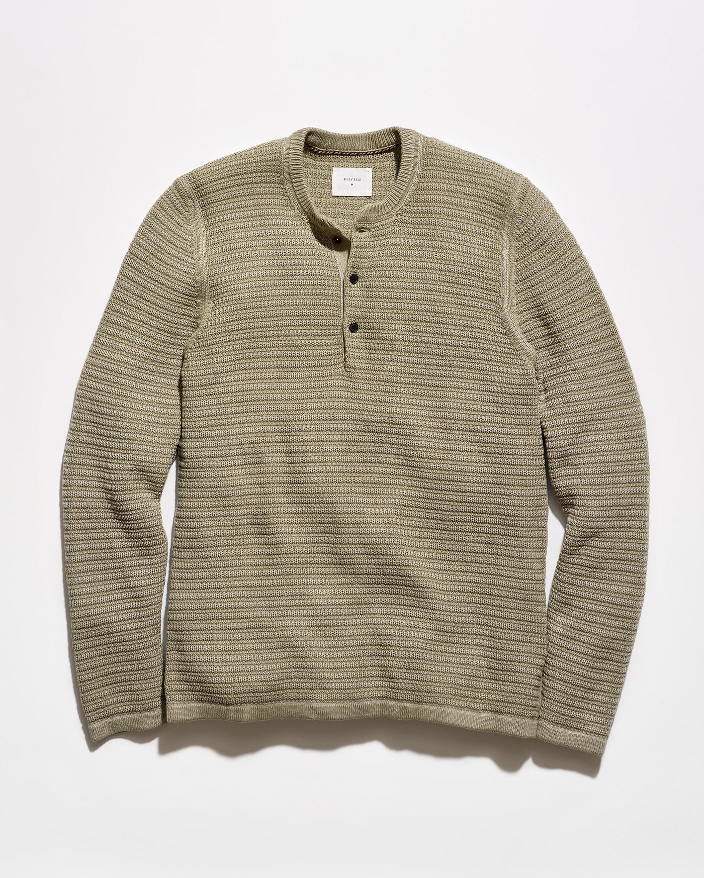 A ribbed knit long-sleeve henley shirt in a muted olive-beige color, featuring a three-button placket and a crew neck, laid flat against a light gray background.