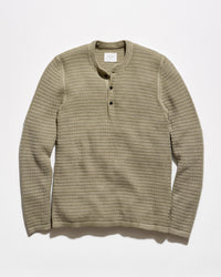A ribbed knit long-sleeve henley shirt in a muted olive-beige color, featuring a three-button placket and a crew neck, laid flat against a light gray background.