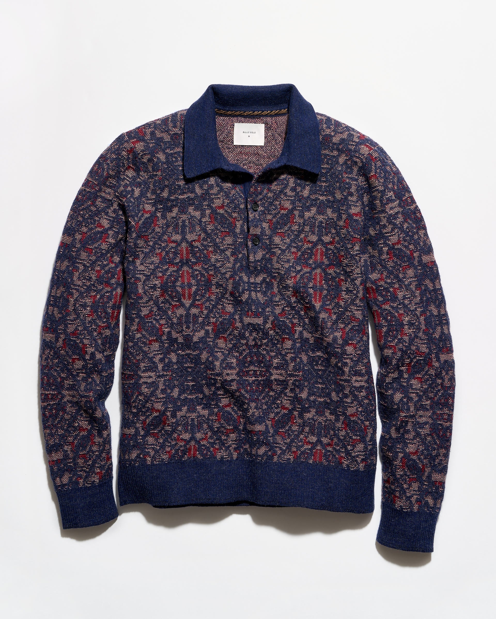 A long-sleeve knit polo-style sweater with an intricate geometric pattern in navy blue, burgundy red, and beige, featuring solid navy ribbed trim on the collar, cuffs, and hem.