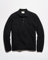 A black long-sleeve knit polo shirt with a textured horizontal rib pattern, laid flat against a clean white background.
