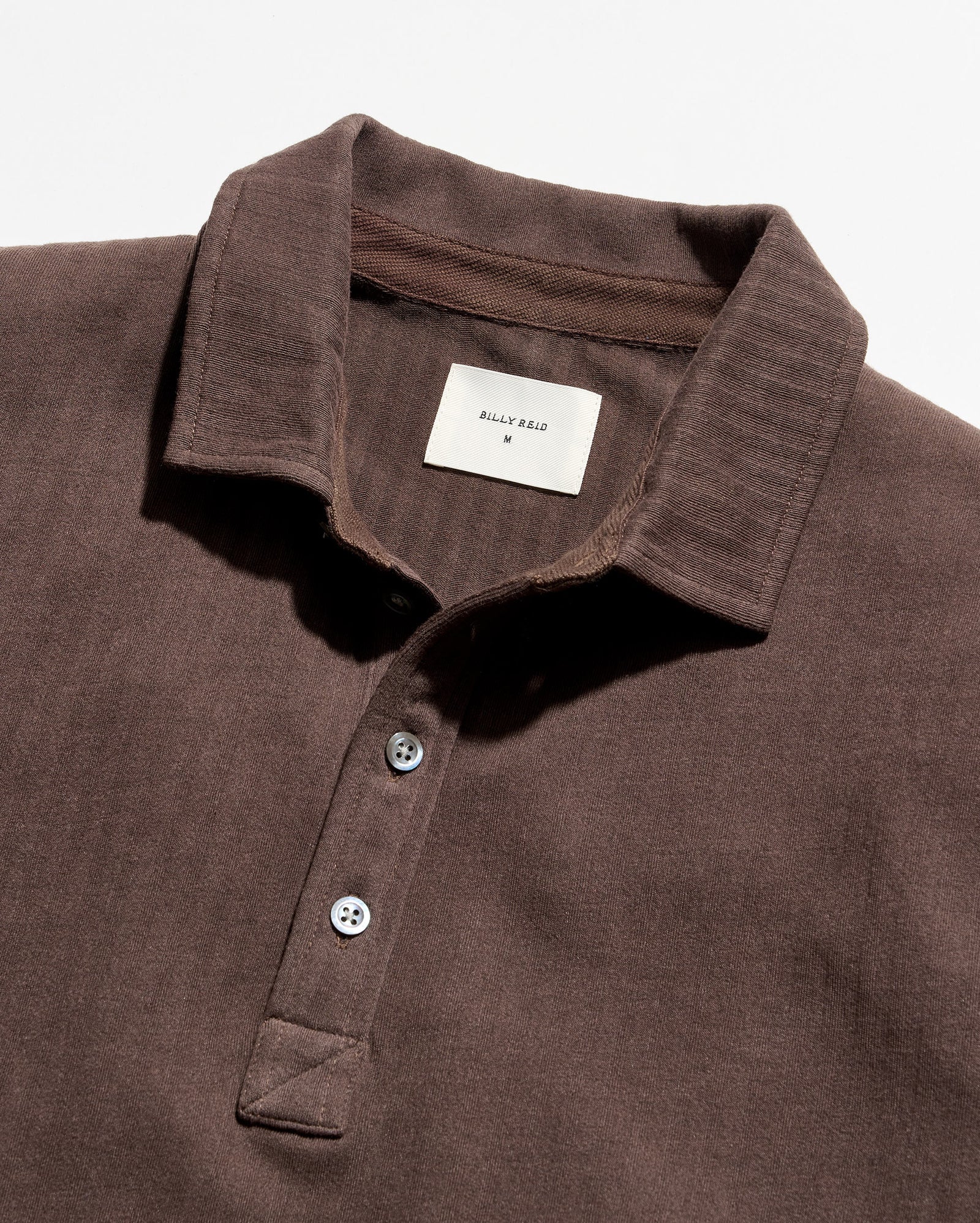Close-up of a dark brown textured polo shirt by Billy Reid, showing the collar, three-button placket, and a white brand label.