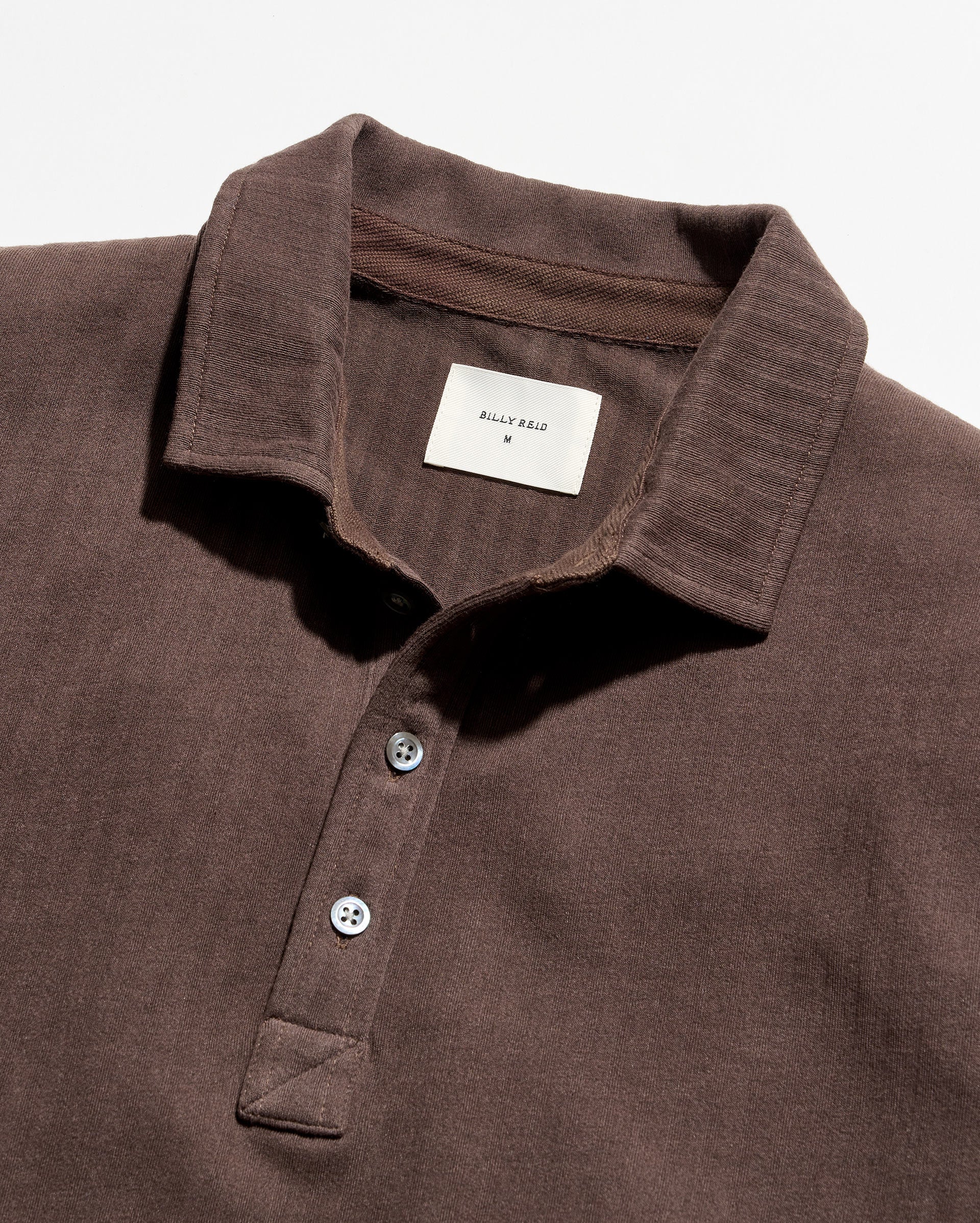 Close-up of a dark brown textured polo shirt by Billy Reid, showing the collar, three-button placket, and a white brand label.