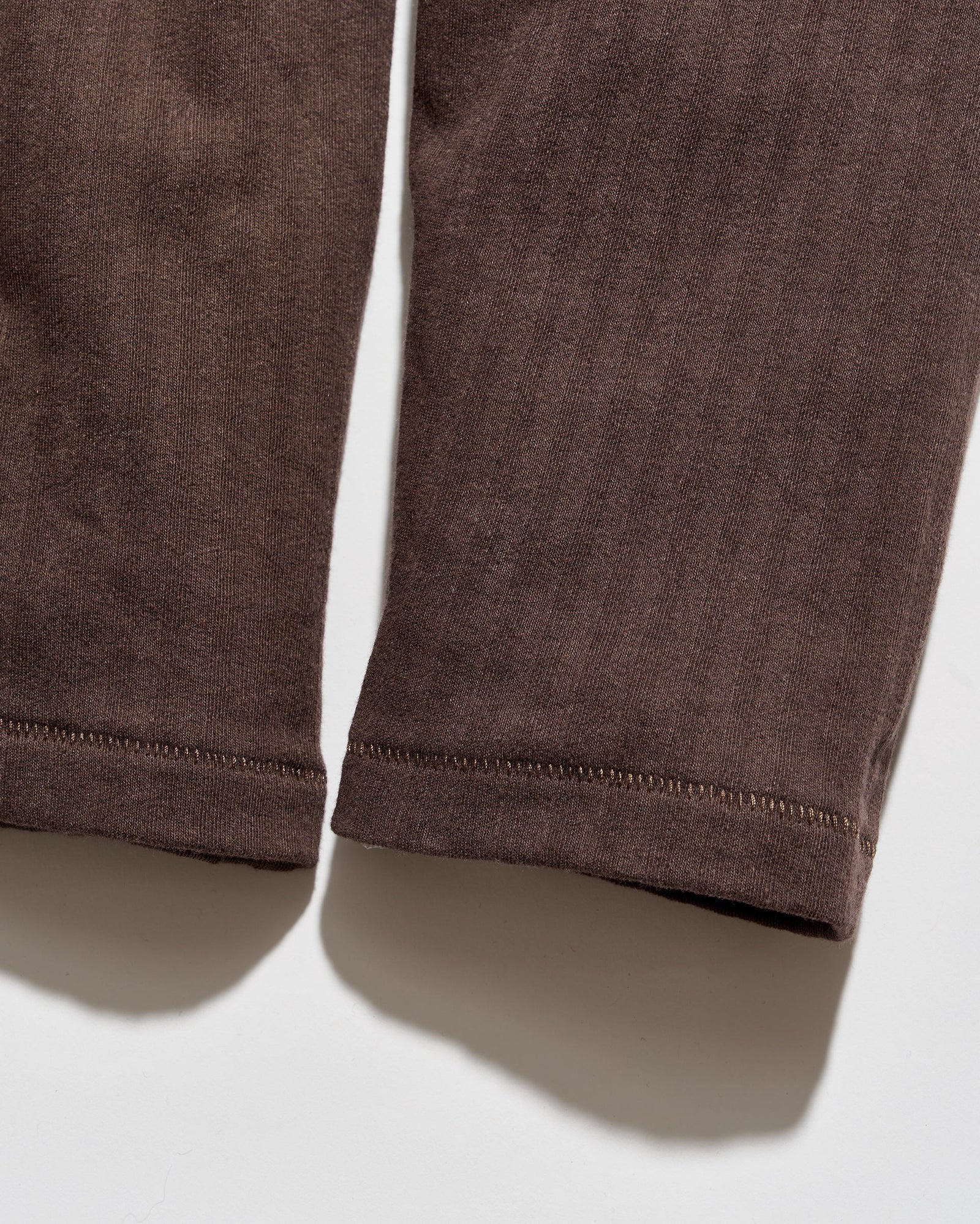 Close-up of the lower legs of dark brown corduroy trousers, showing the ribbed texture and hemstitching against a white background.
