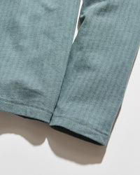 Close-up of a pair of heathered sage green pants or leggings laid flat on a white surface, showing the fabric texture and hem stitching.