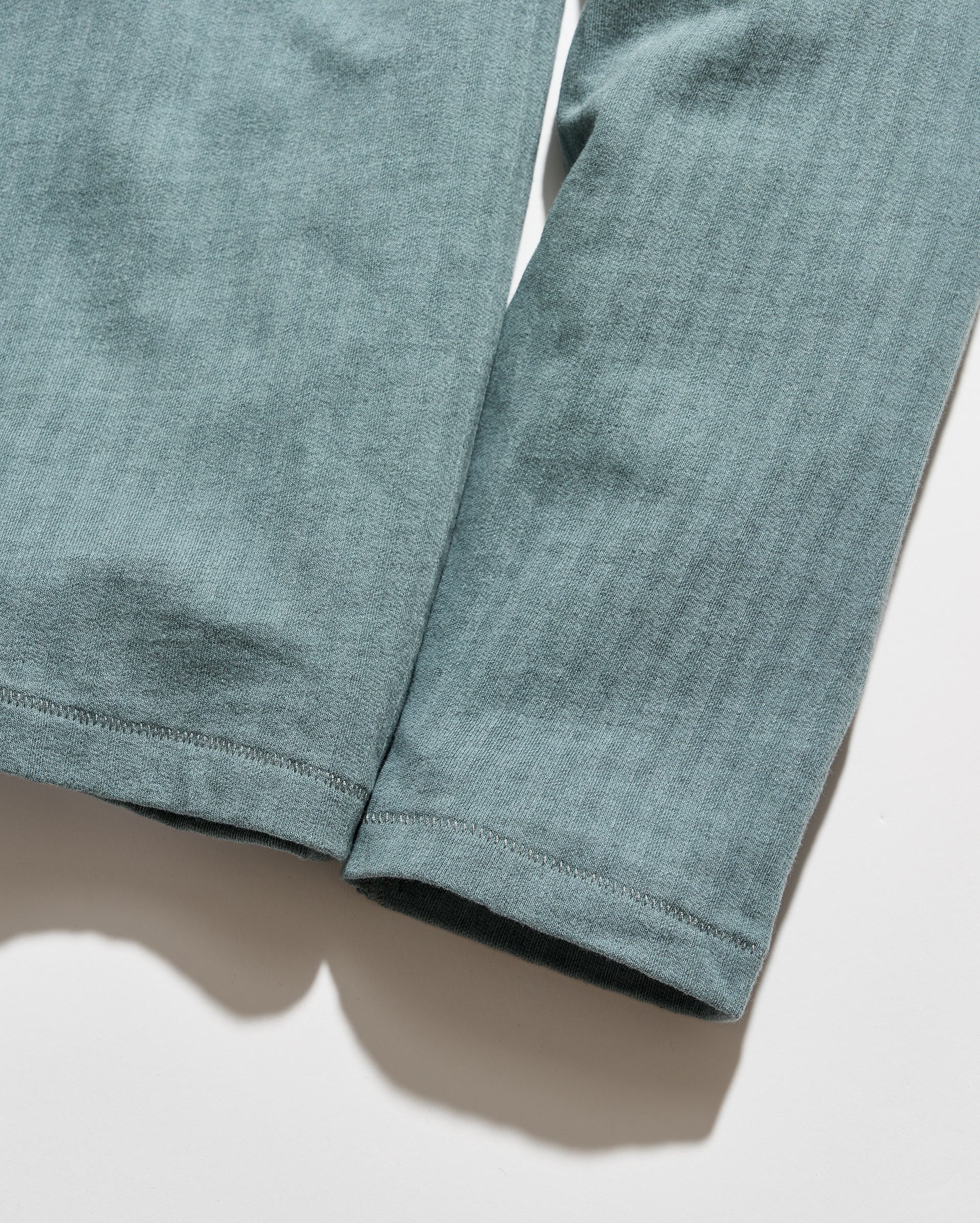 Close-up of a pair of heathered sage green pants or leggings laid flat on a white surface, showing the fabric texture and hem stitching.