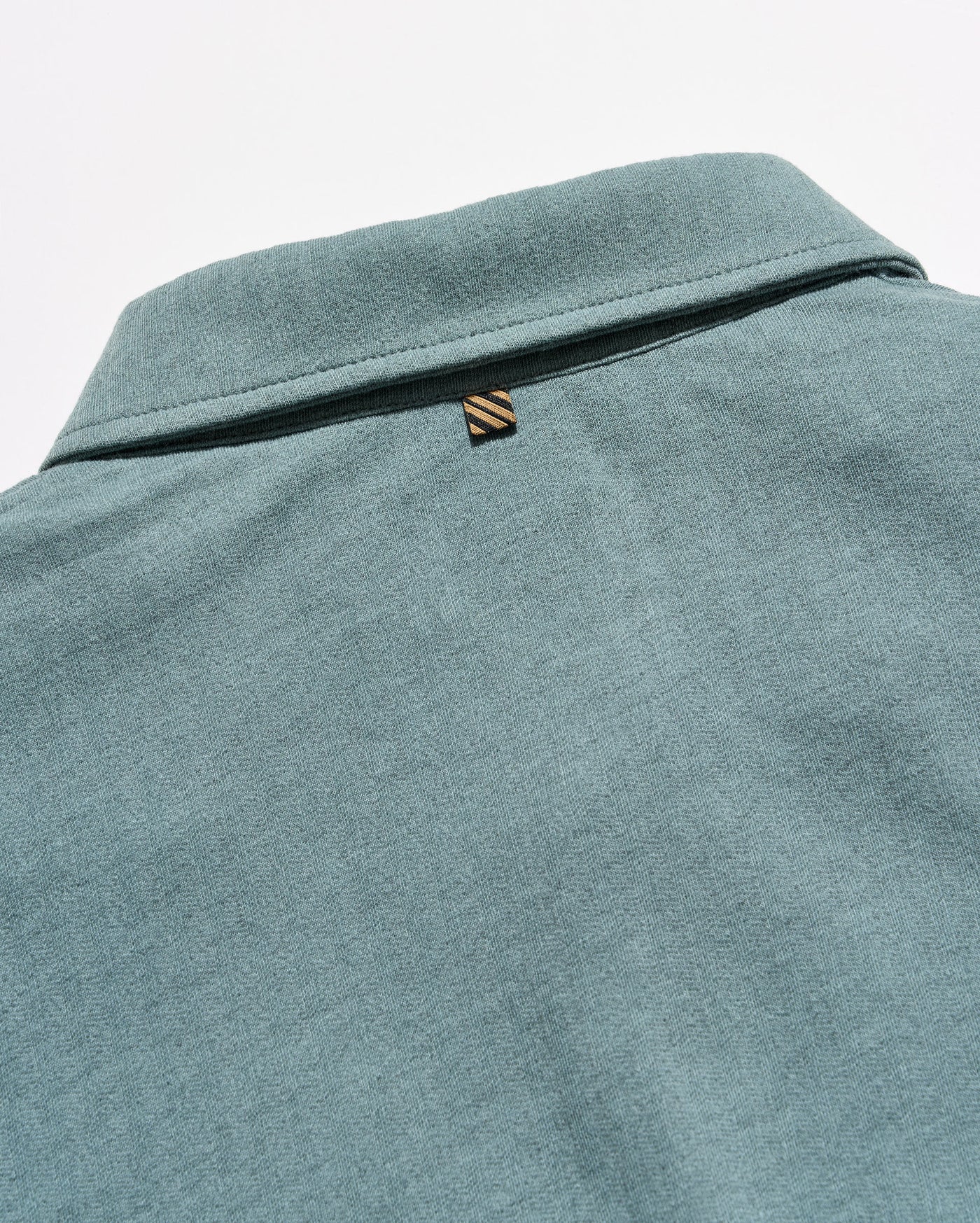Close-up of the back collar of a heathered teal-green polo shirt, featuring a small embroidered striped logo tab.