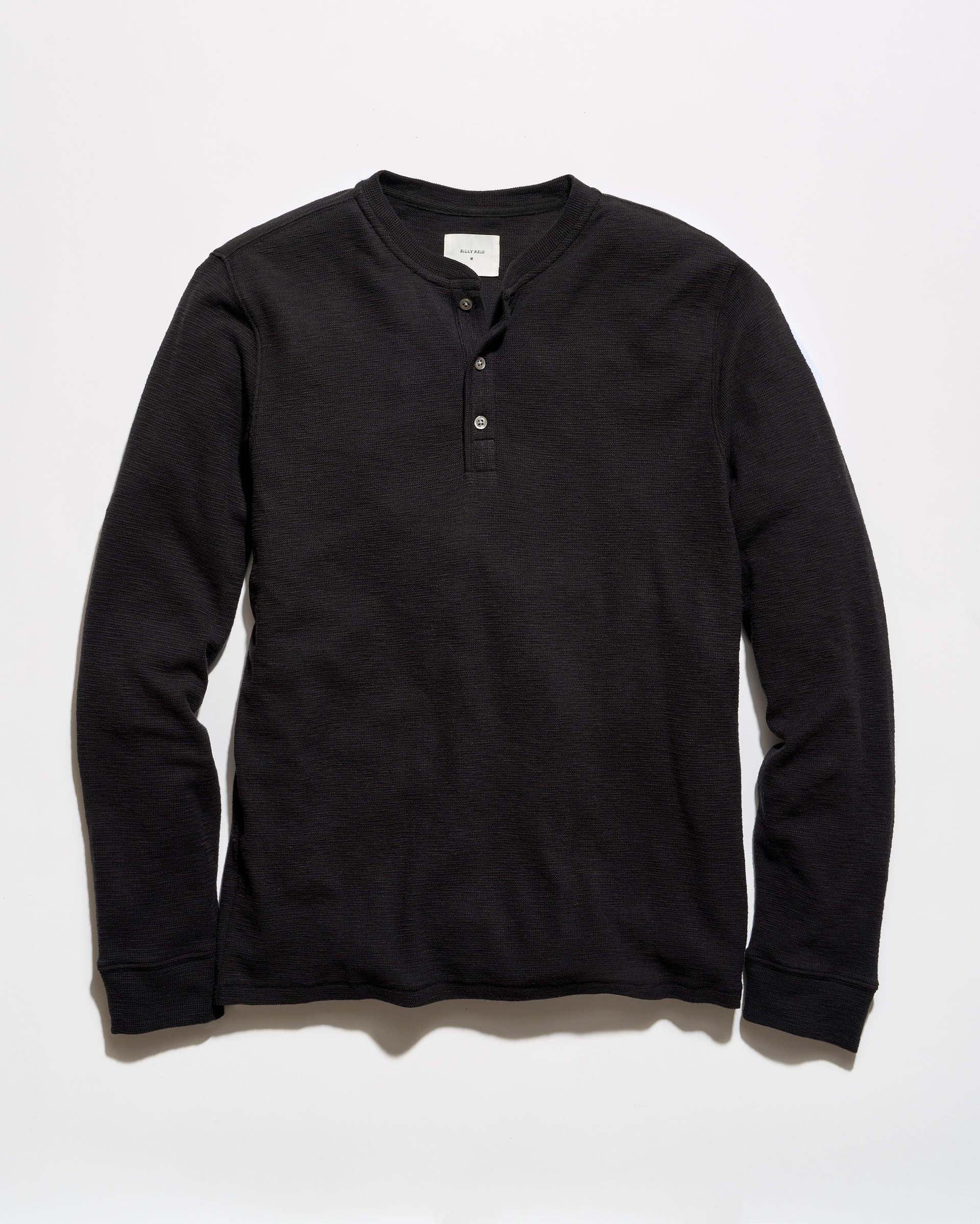 A black long-sleeve henley shirt with a three-button placket, laid flat against a light gray background.