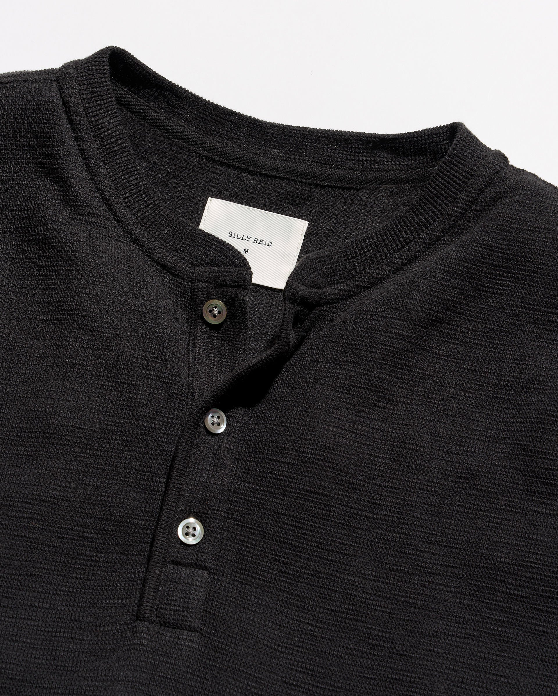 Close-up of a black ribbed Henley shirt with a three-button placket and a white neck label