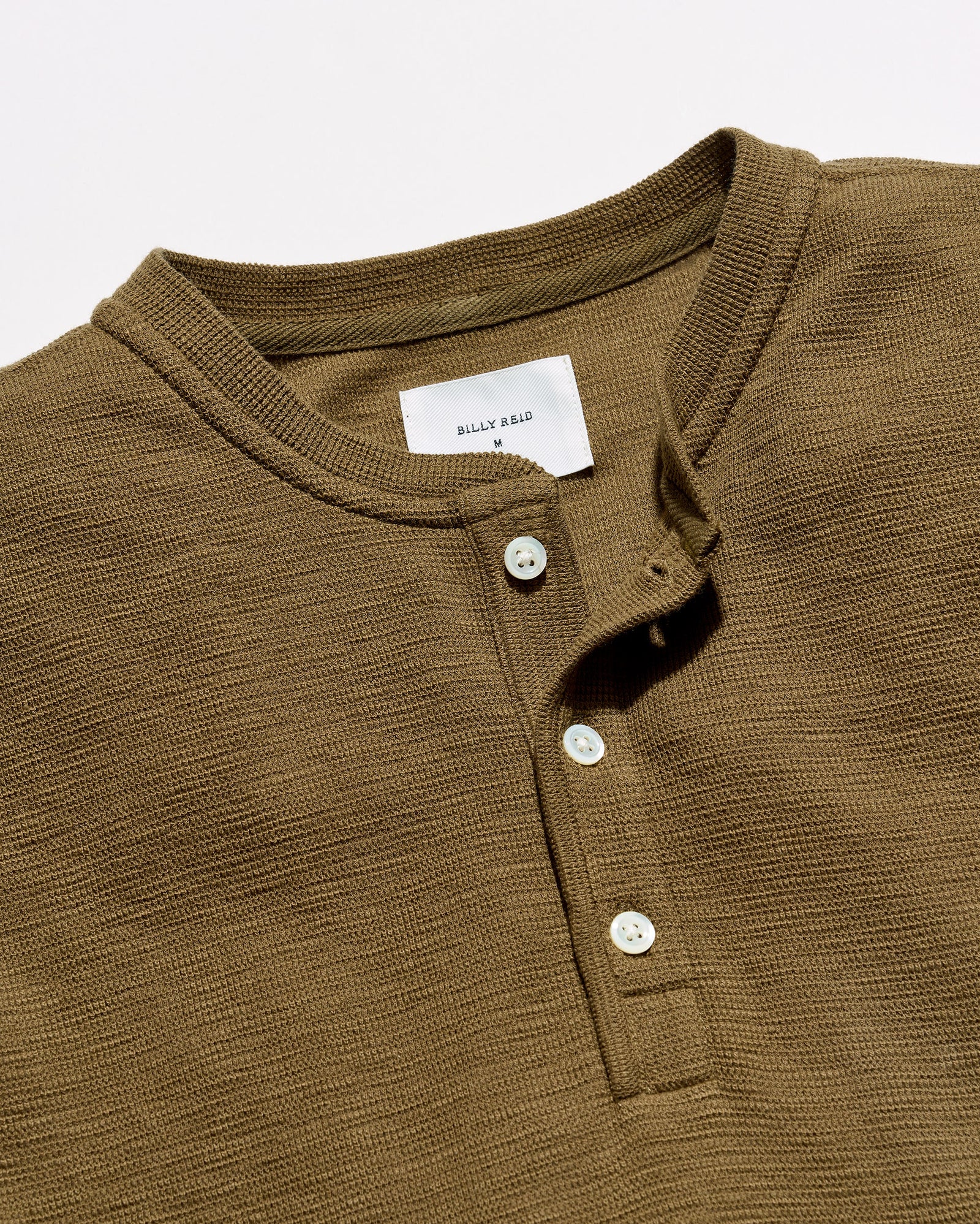Close-up of a ribbed Henley shirt in olive brown with a white button placket and a visible 'BILLY REID' neck label.