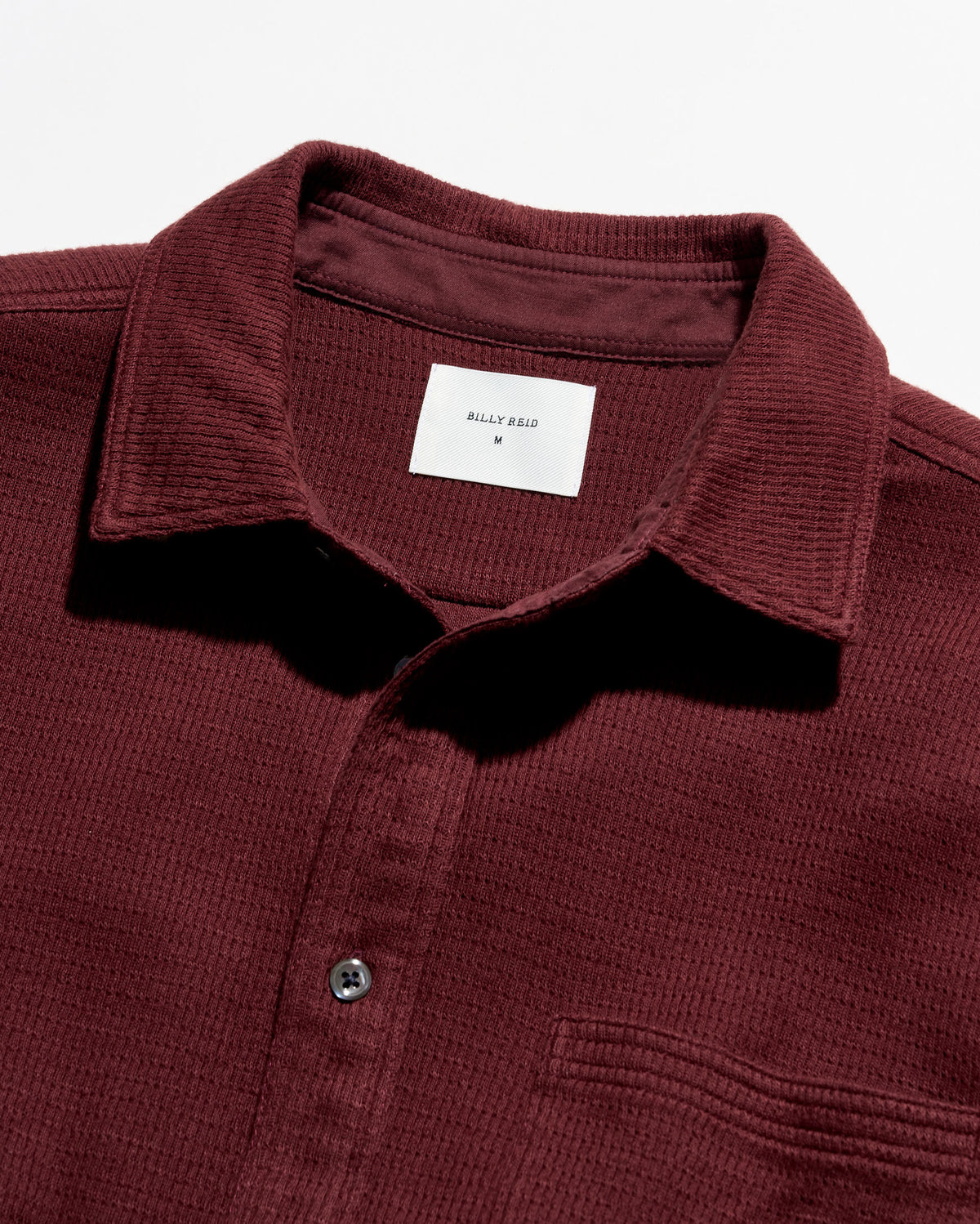 Close-up of a waffle-knit polo shirt collar in burgundy with a white inner neck label reading Billy Reid.