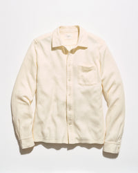 A cream-colored long-sleeve button-up shirt with a single chest pocket, laid flat against a light off-white background.