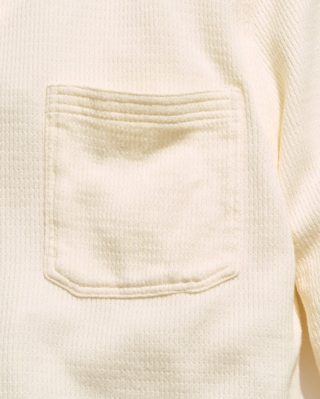 Close-up of a cream-colored waffle-knit garment featuring a square chest pocket with decorative stitching.