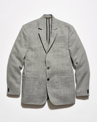 A light gray textured blazer with black tape reinforcement at the back interior, featuring a two-button closure and two front patch pockets, displayed flat against a white background.