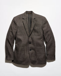 A men's plaid overshirt jacket featuring a navy, beige, and gray tartan pattern, button-up front, and two large diagonal welt pockets on the lower front.