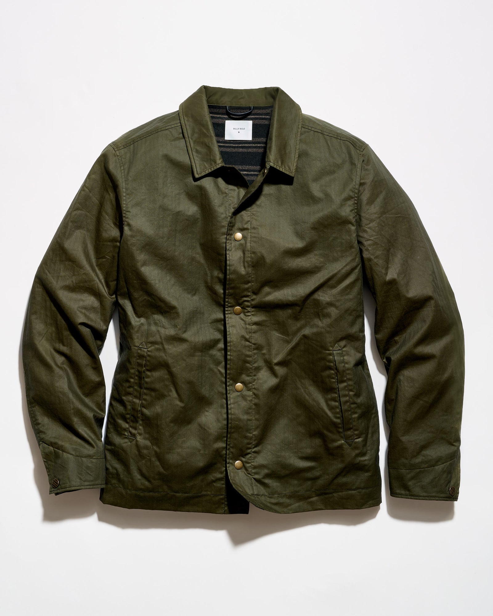 An olive green waxed cotton jacket with a button-up front, laid flat against a white background.