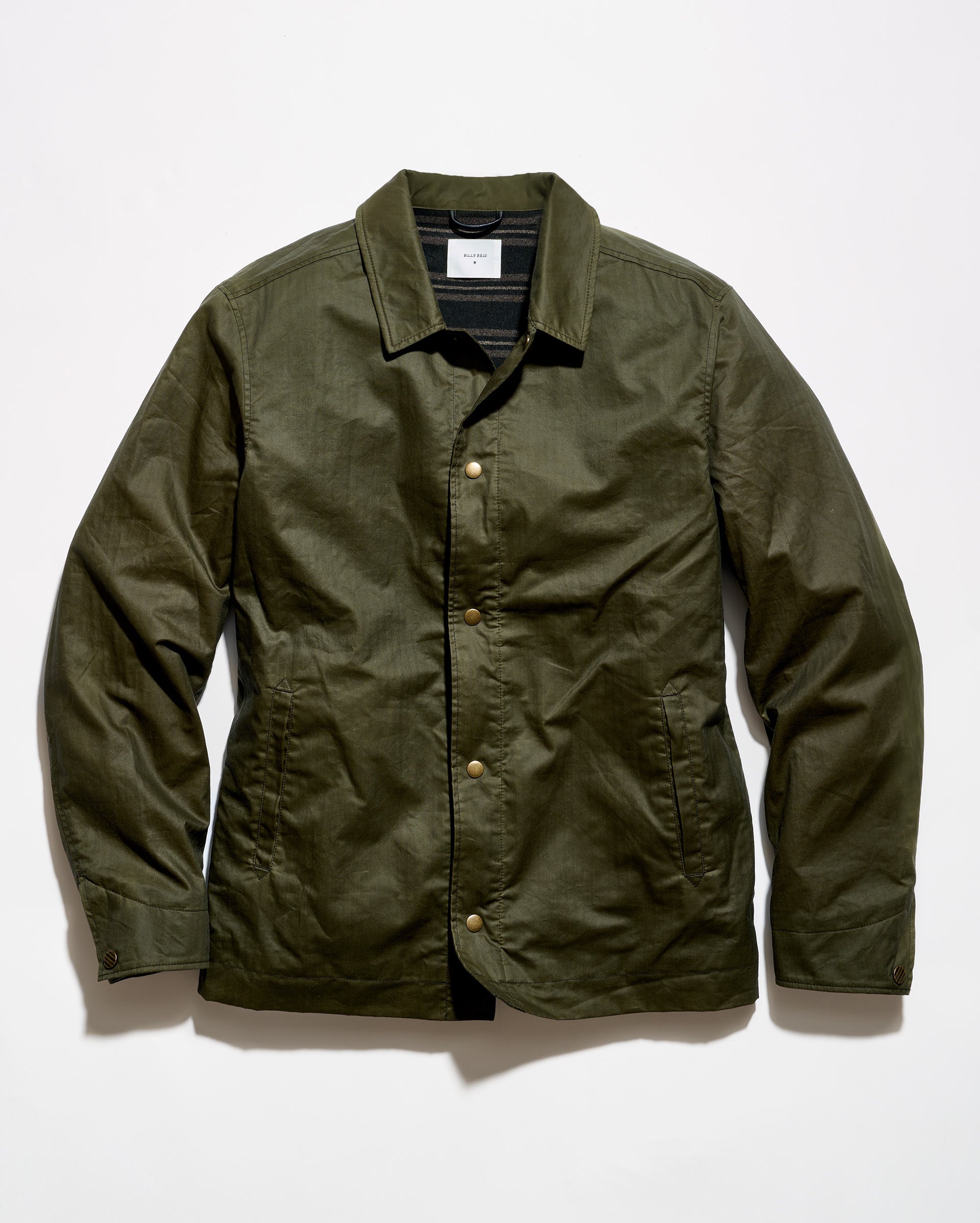 An olive green waxed cotton jacket with a button-up front, laid flat against a white background.