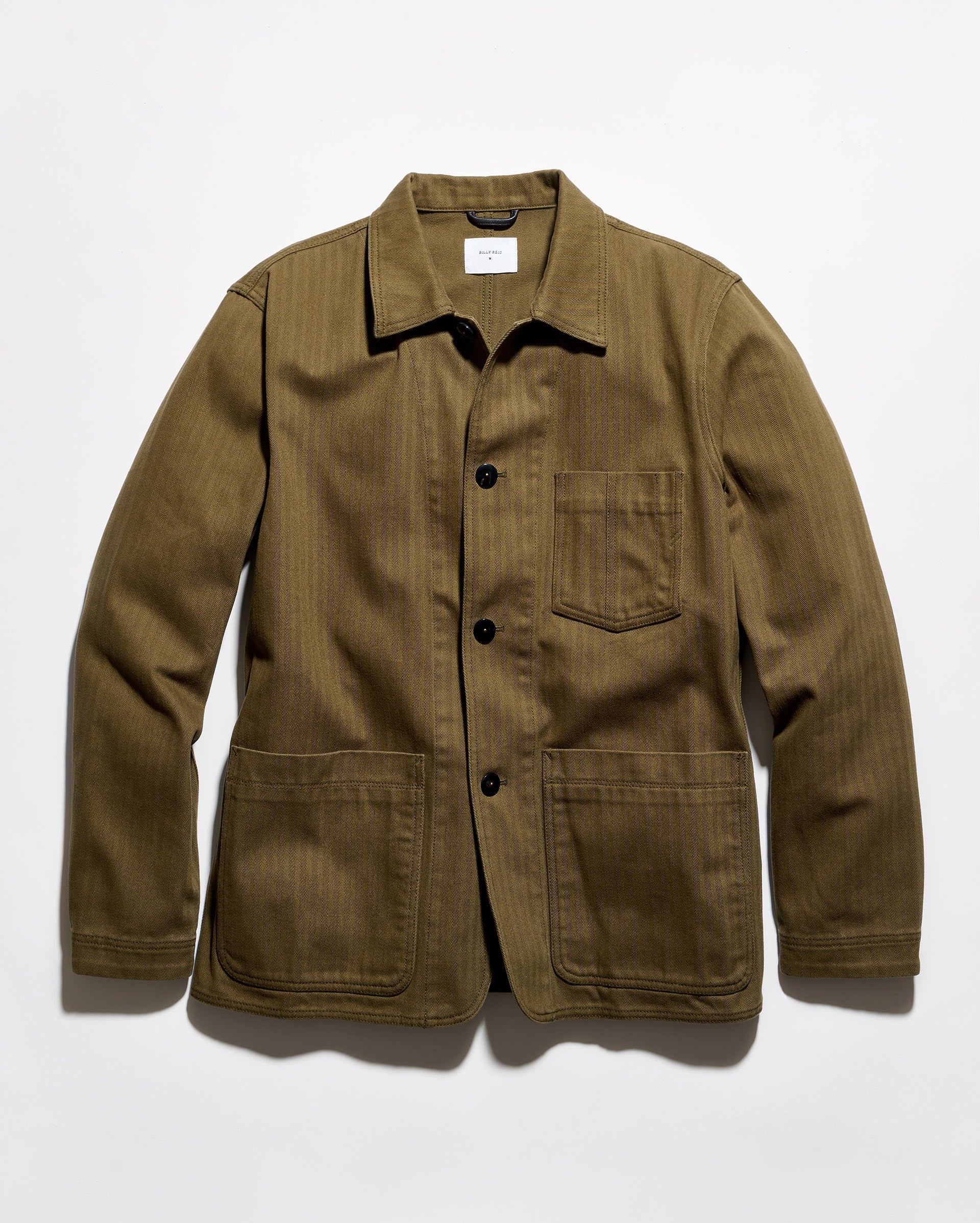 An olive green corduroy utility jacket with a pointed collar, black snap-button front, and four front pockets, laid flat against a white background.